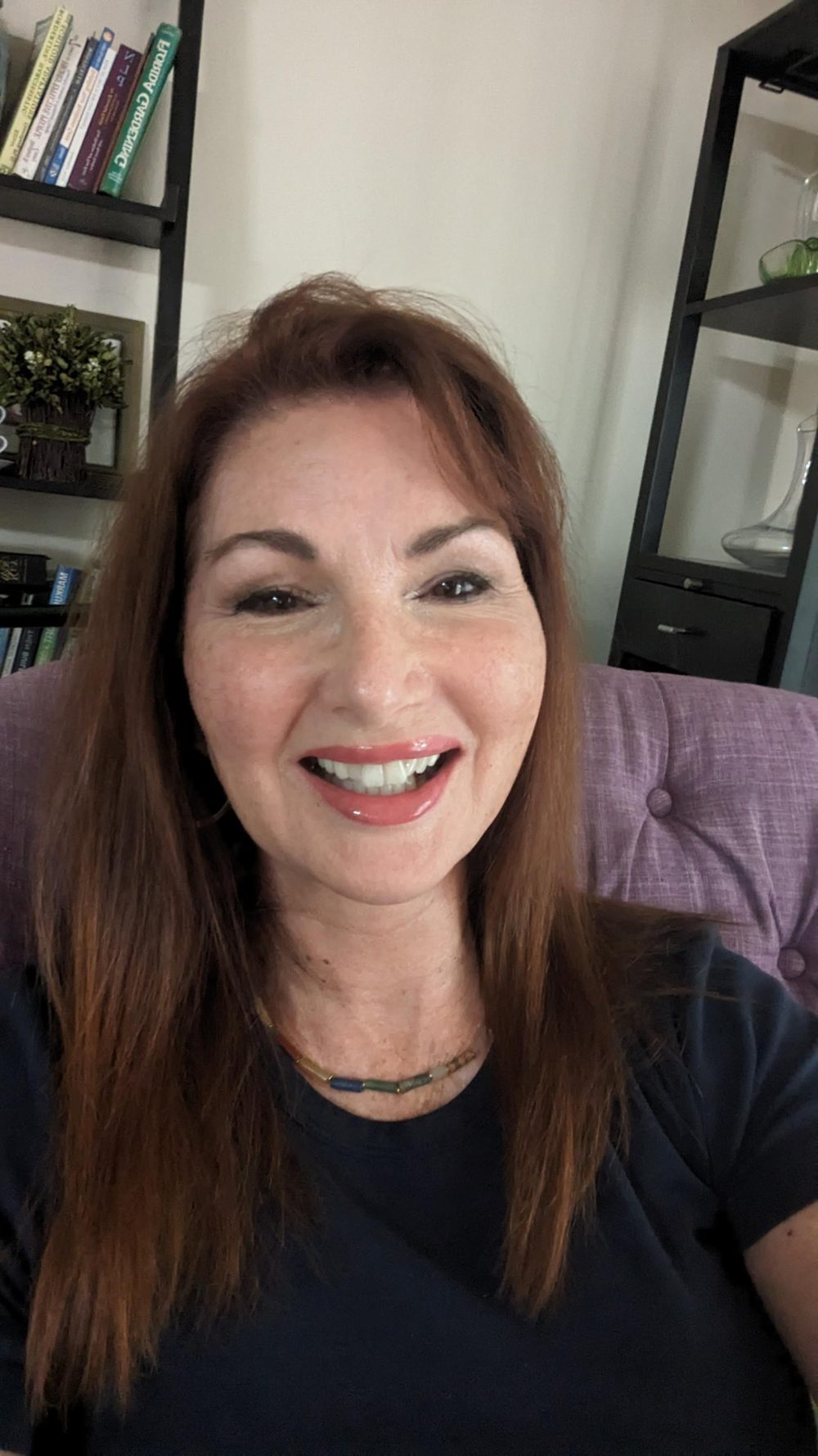 Tracy laughing, wearing a navy top, sitting in a lavender armchair at home