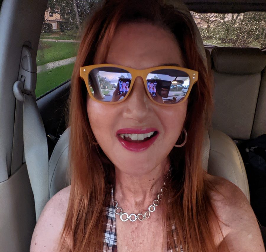 Tracy grinning in yellow-framed mirrored sunglasses in her car